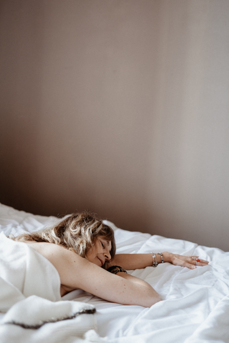 Femme allongée sur un drap blanc, la lumière naturelle enveloppant ses courbes.