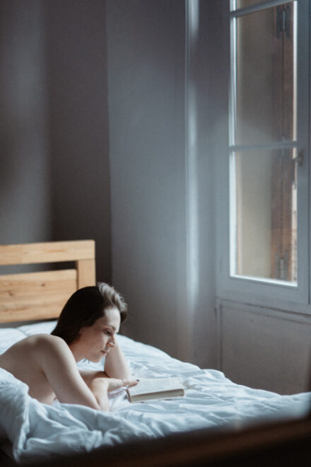 Femme allongée sur un lit, lisant un livre, une atmosphère feutrée et élégante.