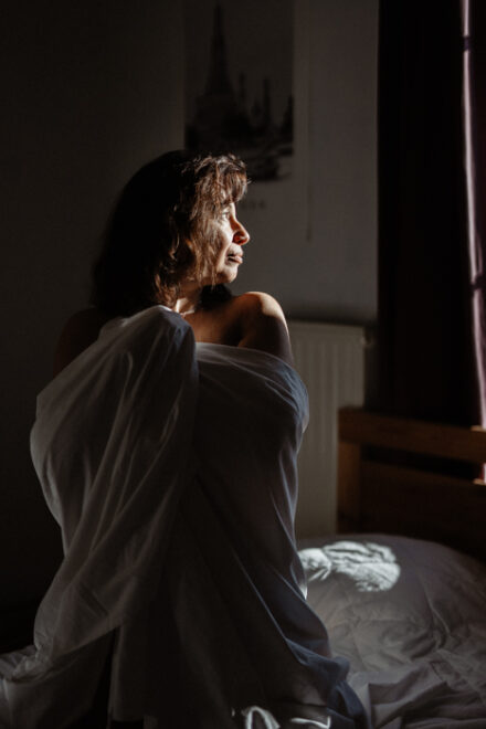 Femme dans des draps blancs, baignée par la lumière du matin.