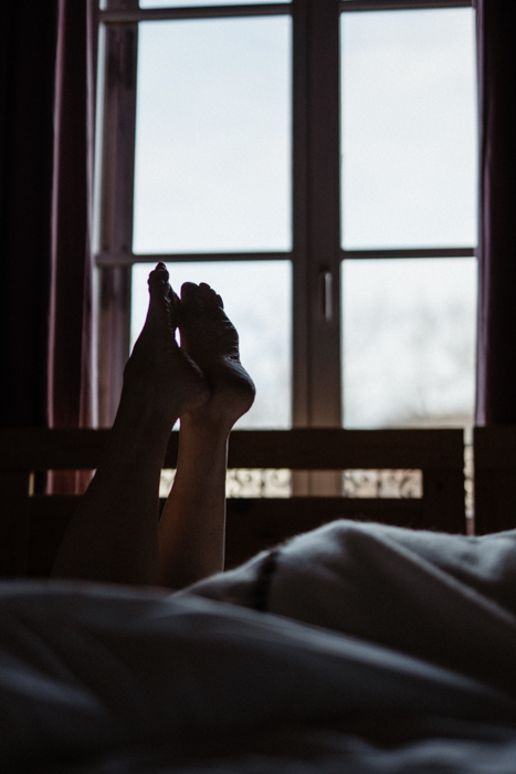 Femme couverte d’un drap léger, jouant avec ses pieds avec la lumière naturelle.